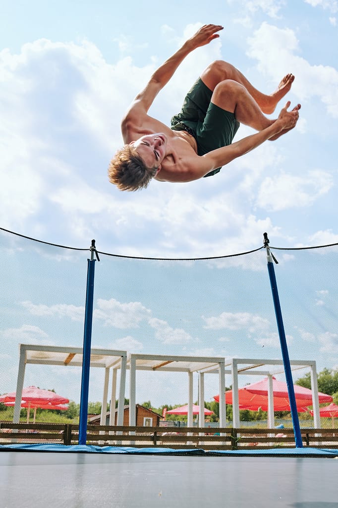 Young topless sportsman in green shorts jumping over trampoline outside